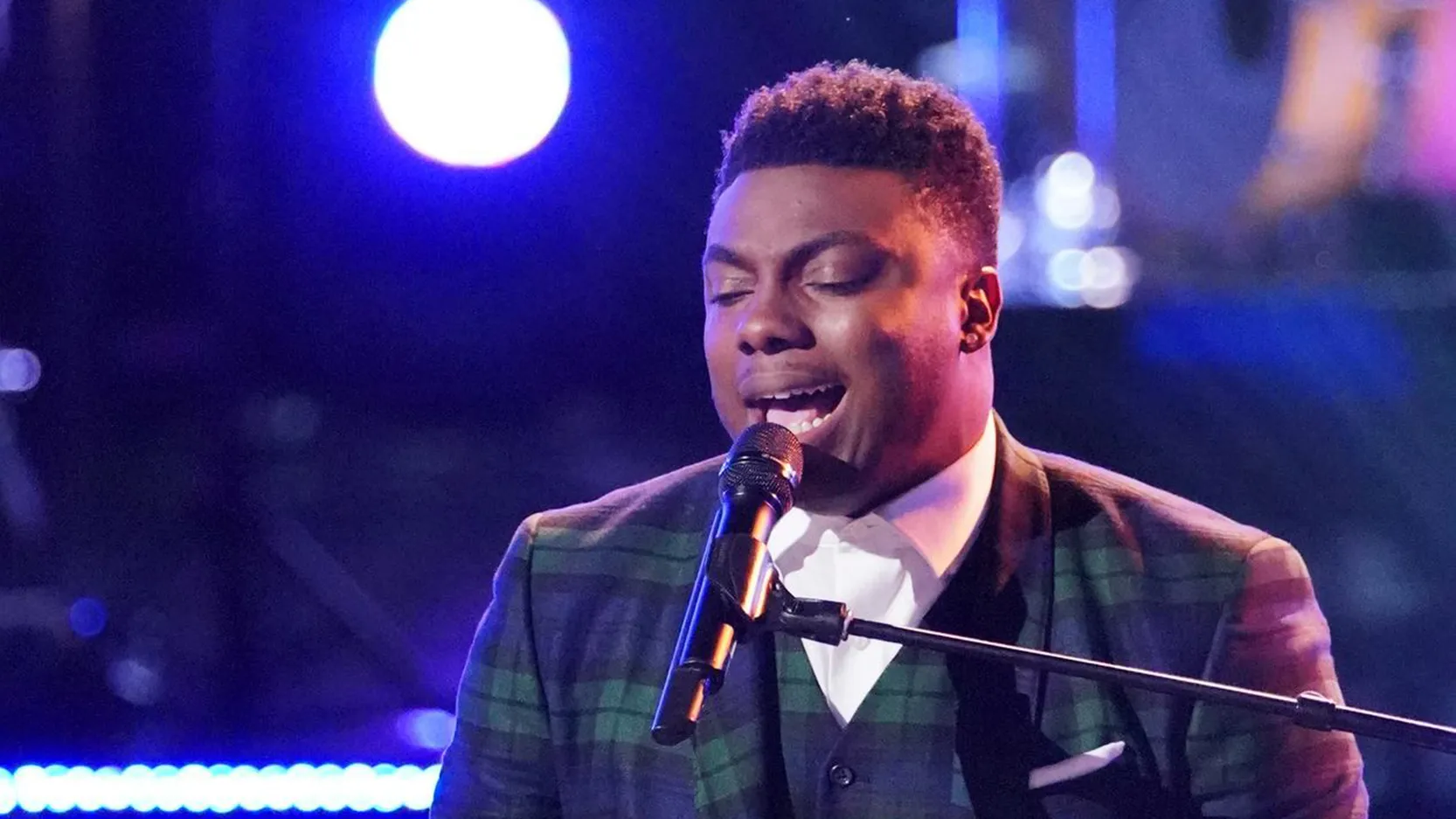 Kirk Jay singing at the piano in a green plaid blazer