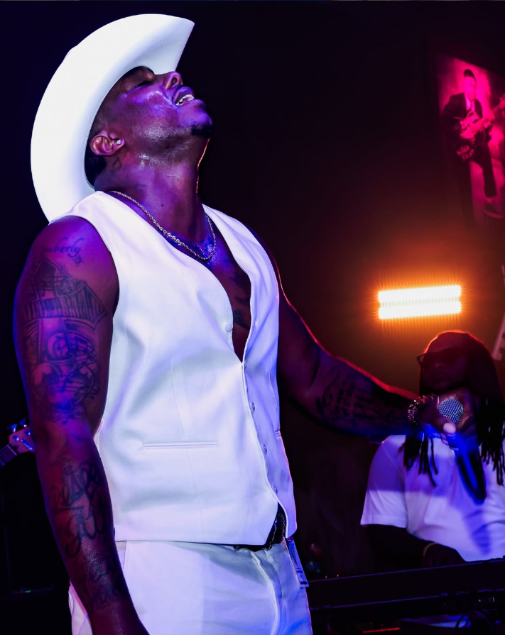 Kirk Jay singing in a white cowboy hat and white vest under stage lights